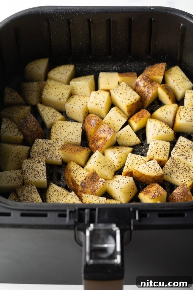 Russet Potatoes Ultimate Recipe and Cooking Tips 9 Raw pieces of cubed potato in the basket of an air fryer, seasoned with salt and pepper.