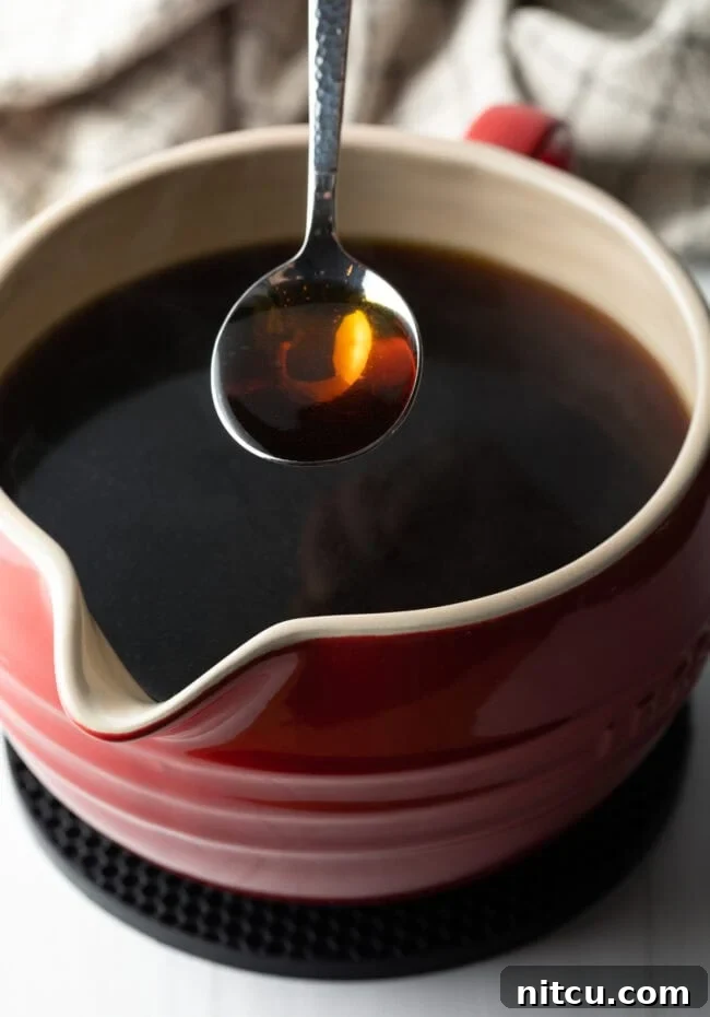 Golden Beef Essence 11 A spoon holding consomme over a ceramic bowl filled with consomme.