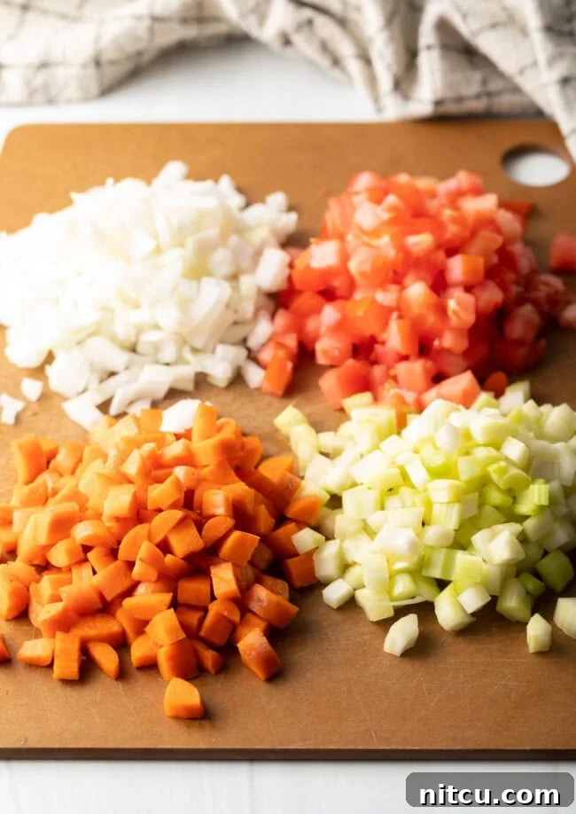 Golden Beef Essence 4 Mirepoux: diced tomatoes, white onion, celery, and carrots on a cutting board.