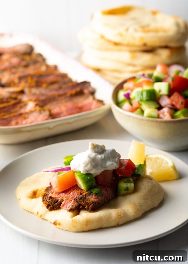 Authentic Street Style Beef Shawarma 13 Close view flatbread naan beef shawarma wrap topped with chopped cucumbers, tomatoes, red onion and tzatziki sauce.