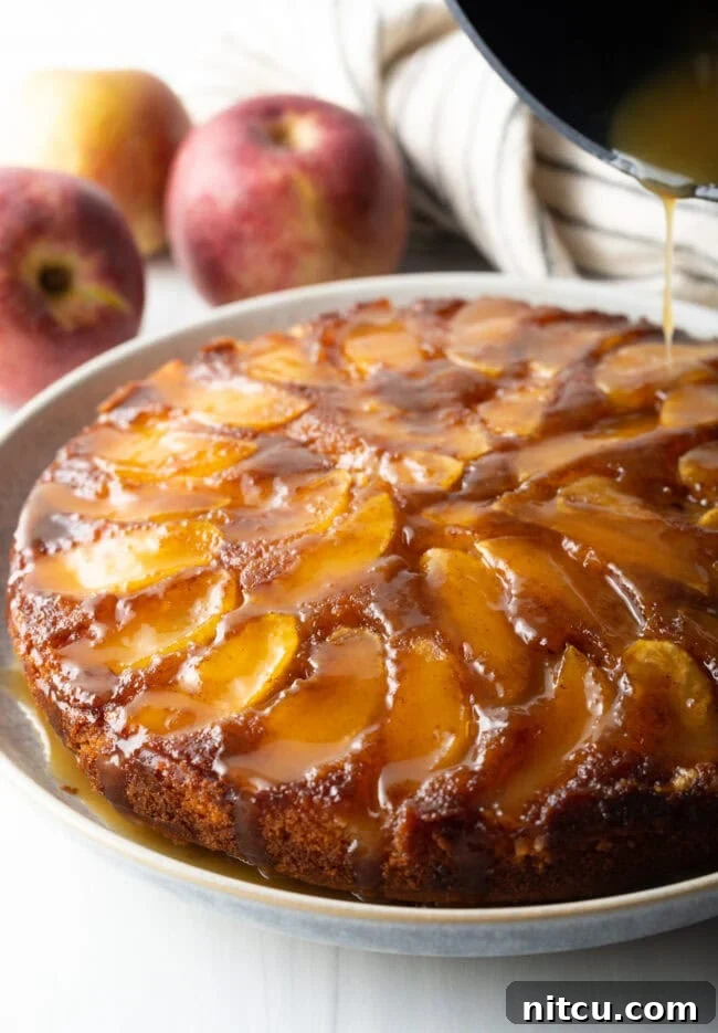 Effortless Apple Caramel Flip Cake 2 Upside down apple cake on a serving plate with whiskey sauce being poured on top.
