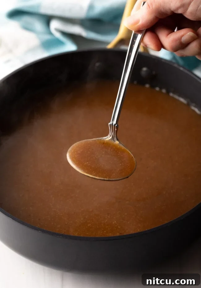 Metal ladle filled with glistening brown gravy held up to the camera, showing its smooth consistency.