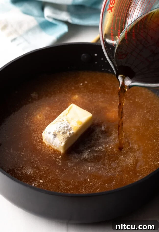 Beef broth being poured into a deep skillet containing the butter and cornstarch mixture, being whisked vigorously.