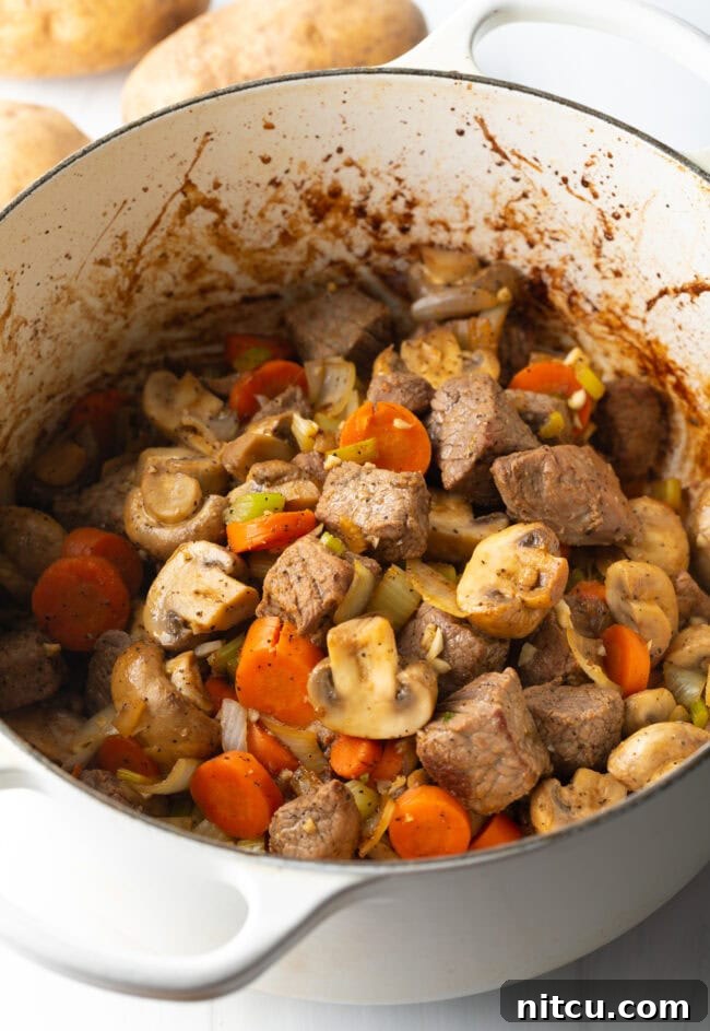 Kitchen Sink Stew 7 Chopped carrots, celery, onion, mushrooms, and potatoes with chunks of beef in a pot.