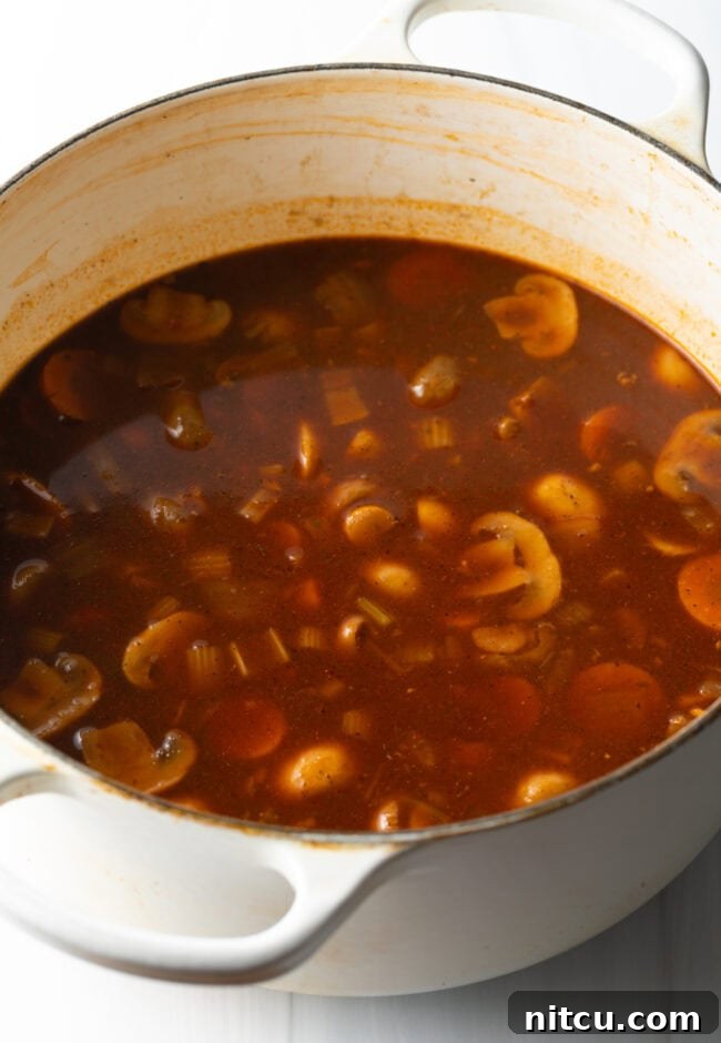 Kitchen Sink Stew 8 Adding mushrooms and in a tomato broth in a pot.