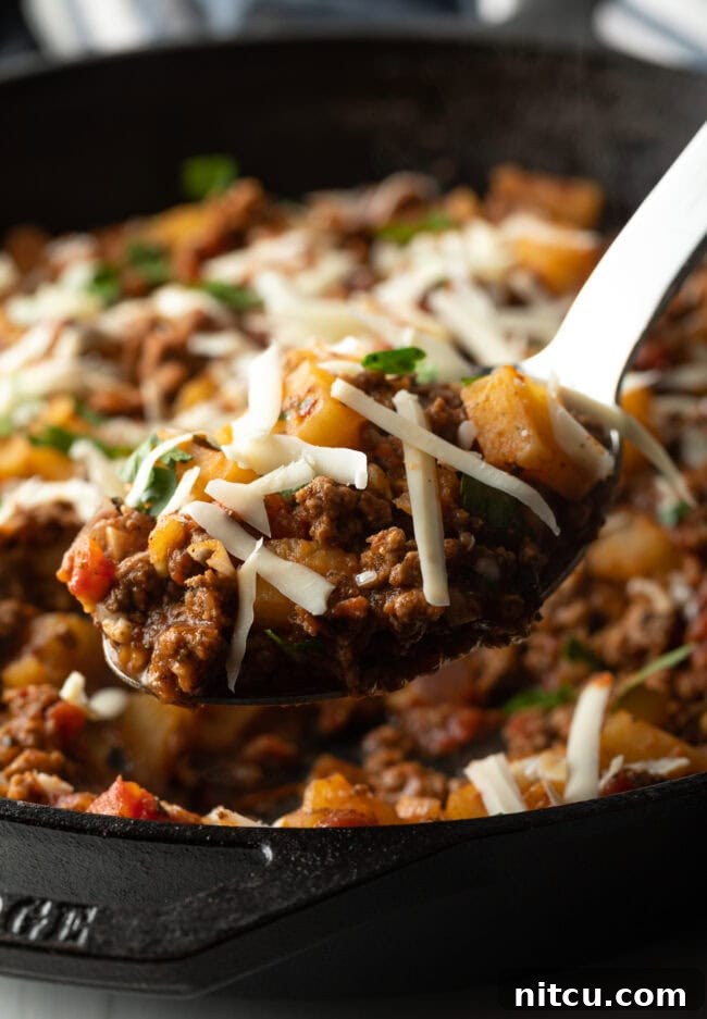 Tuscan Beef & Potato Skillet 11 Metal spoon with potatoes and ground meat, topped with shredded parmesan cheese.