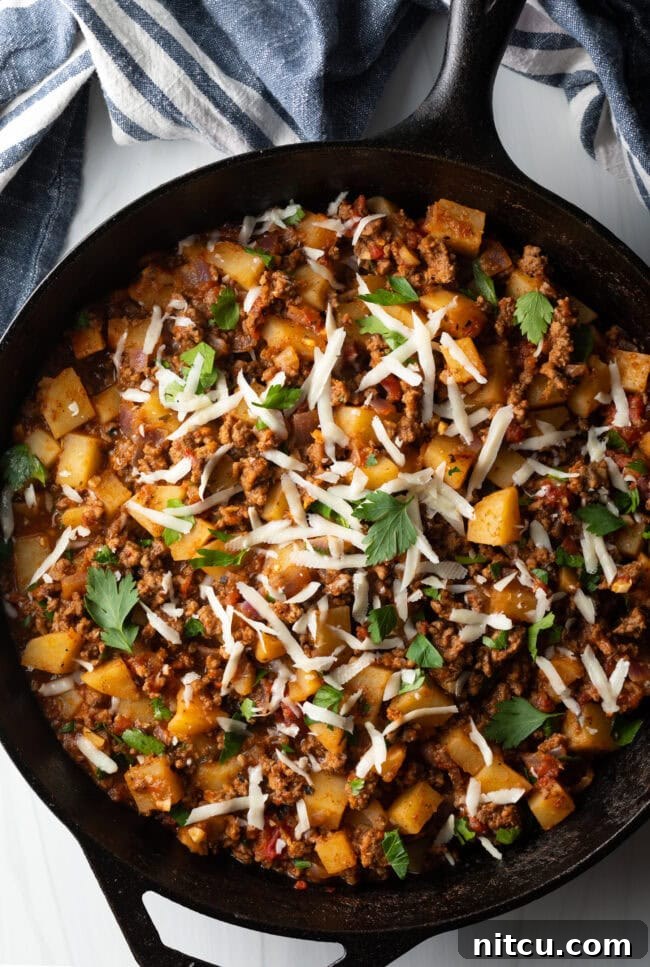 Tuscan Beef & Potato Skillet 3 Top down view ground beef and potatoes, topped with shredded parmesan cheese in a skillet.