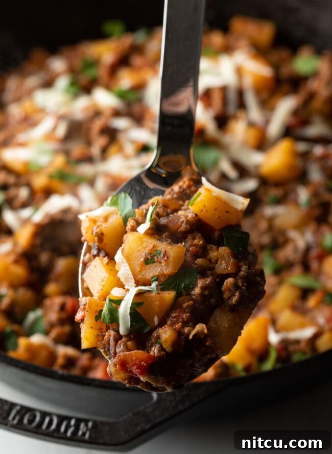 Tuscan Beef & Potato Skillet 4 Metal spoon with ground beef and potatoes, topped with shredded parmesan cheese.