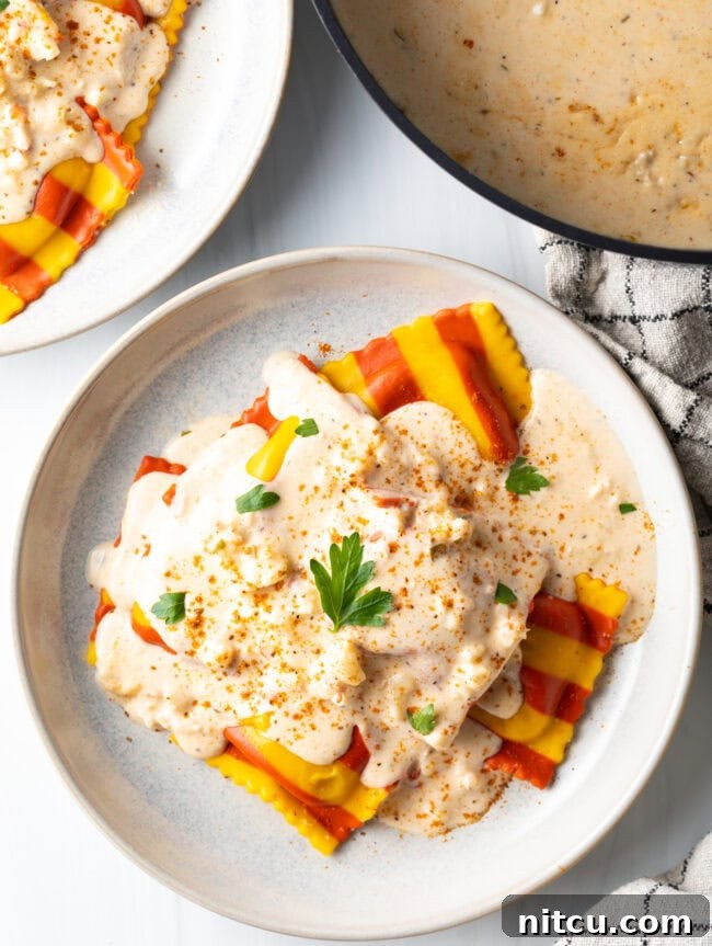 Top down view of a white plate with yellow and red striped ravioli, covered in creamy lobster sauce and sprinkled with parsley.