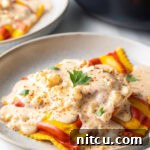 White plate with yellow and red striped lobster ravioli, covered in a rich cream sauce and sprinkled with parsley.