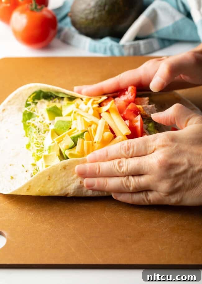 Your New Favorite Chicken Wrap 9 Two hands holding ingredients into the loaded tortilla while starting to roll into a wrap.