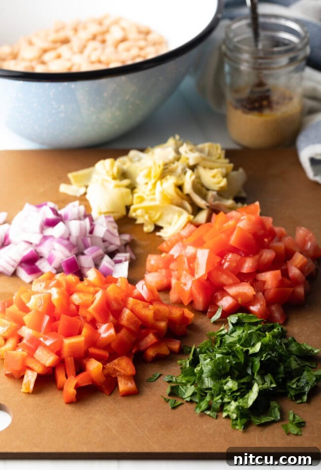 Ingredients prep: chopped red onion, artichoke hearts, tomatoes, red bell pepper, and parsley on a brown cutting board.
