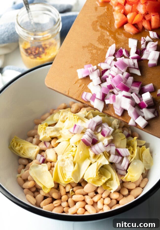 Adding artichoke hearts and diced onion to bowl with beans.