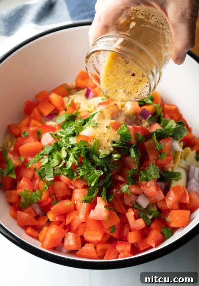 Hand poring vinaigrette dressing from a glass jar onto the chopped ingredients in a bowl.