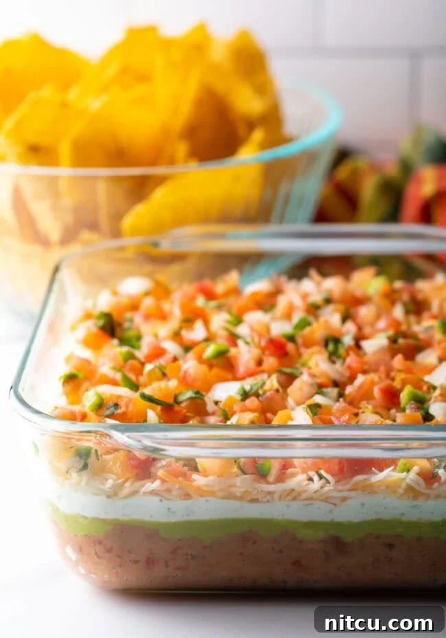 Fiesta Bean Stack 2 Glass square baking dish with layered Mexican bean dip. A bowl of tortilla chips is in the background.
