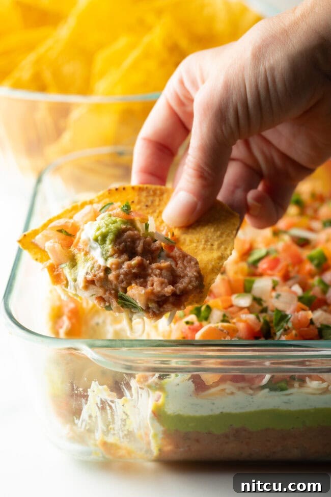 Fiesta Bean Stack 4 Close view of tortilla with a hand using a chip to scoop the 5 layer bean dip.