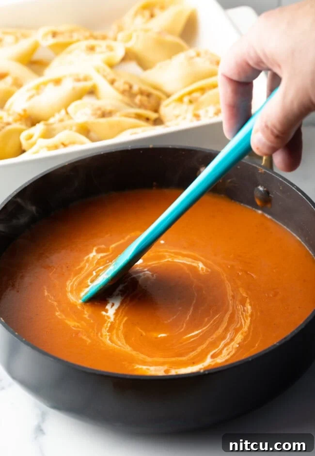 Ocean's Bounty Stuffed Shells 12 Hand with blue spatula stirring cheese mixture in a saucepan.