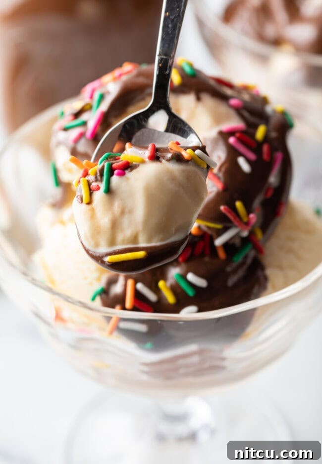 Metal spoon with a scoop of vanilla ice cream, topped generously with homemade chocolate sauce and colorful sprinkles.