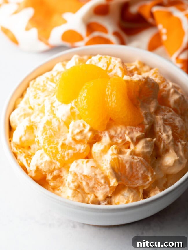 Zesty Orange Ambrosia 2 Top down view of orange fluff salad recipe in a white bowl, garnished with 3 slices of oranges.