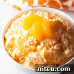 Zesty Orange Ambrosia 12 Top down view of mandarin orange fluff salad in a white bowl, garnished with 3 slices of oranges.
