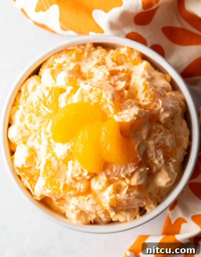 Zesty Orange Ambrosia 4 Top down view of mandarin orange salad in a white bowl, garnished with 3 slices of oranges.