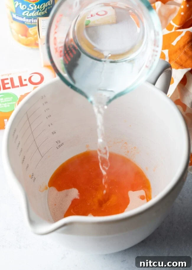 Zesty Orange Ambrosia 6 Water being added from a glass measuring cup into a white mixing bowl.