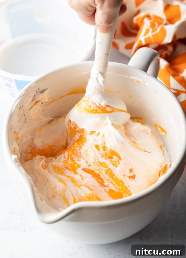 Zesty Orange Ambrosia 8 White bowl, orange fluff being mixed by white spatula.