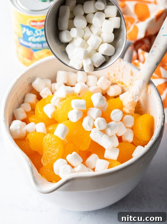 Zesty Orange Ambrosia 9 Adding mini marshmallows to the white mixing bowl with fluffy and oranges.