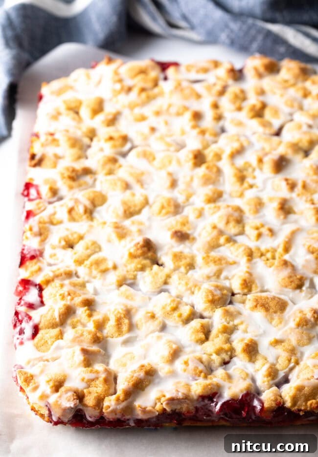 Sweet Cherry Crumble Bars 12 A baked pan of cherry pie bars, showing the bubbly, golden-brown topping and rich red cherry filling peeking through, ready for glazing.