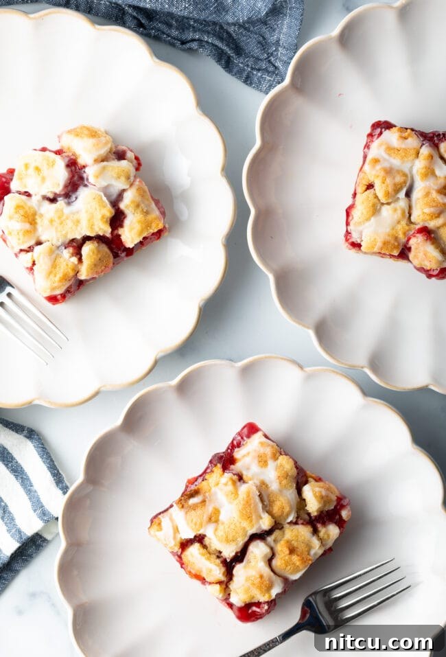 Sweet Cherry Crumble Bars 4 Three pieces of cherry pie bars arranged individually on elegant white scalloped plates, highlighting their golden crust and vibrant cherry filling.