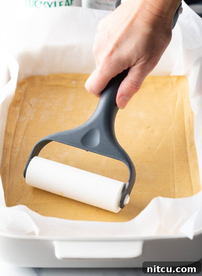 Sweet Cherry Crumble Bars 7 A hand uses a pastry roller to smooth out a rectangle of pie dough into an even layer in a baking pan, creating the base for the bars.