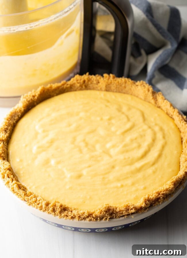 Close-up of the smooth, golden mango custard filling poured evenly into the graham cracker crust, ready for baking.