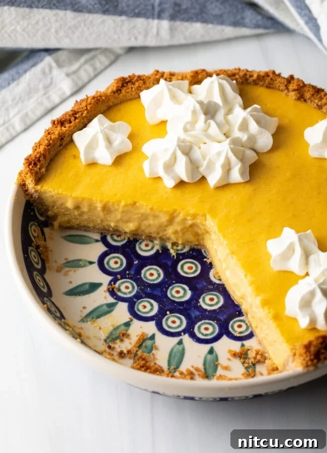 A beautifully crafted mango pie with a generous portion already served, revealing the golden custard filling and crisp graham cracker crust.