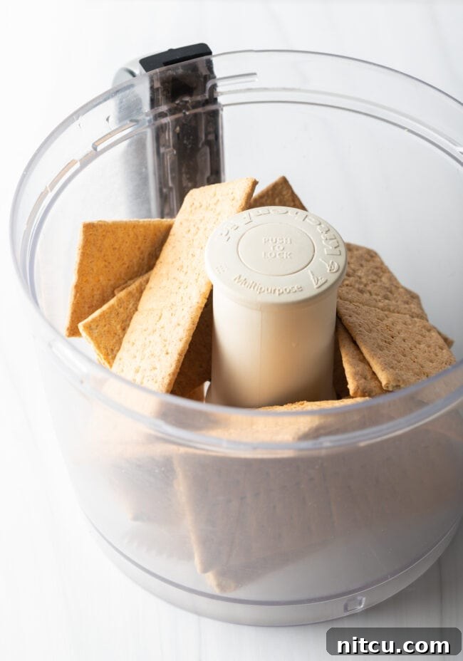 Several sheets of graham crackers being placed into a food processor bowl, ready to be crushed for the pie crust.