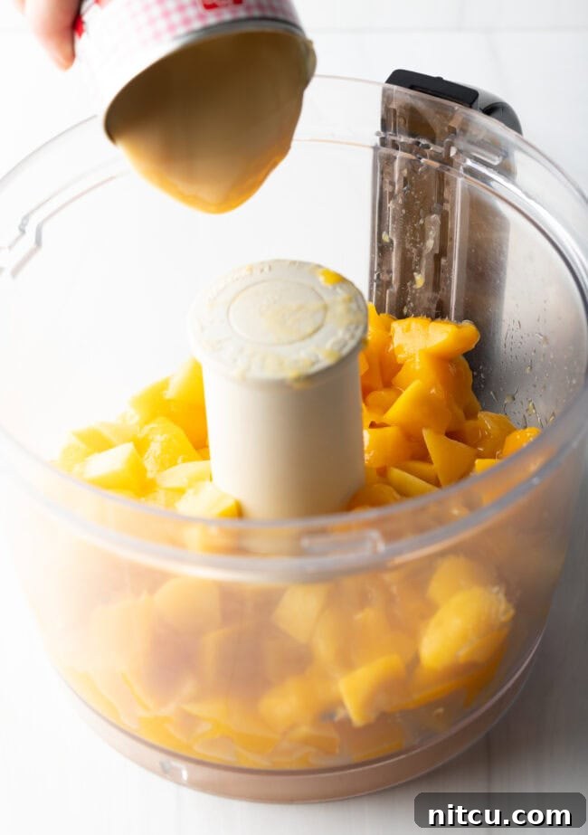 Fresh mango chunks placed inside a food processor bowl, ready to be blended into a smooth purée for the pie filling.