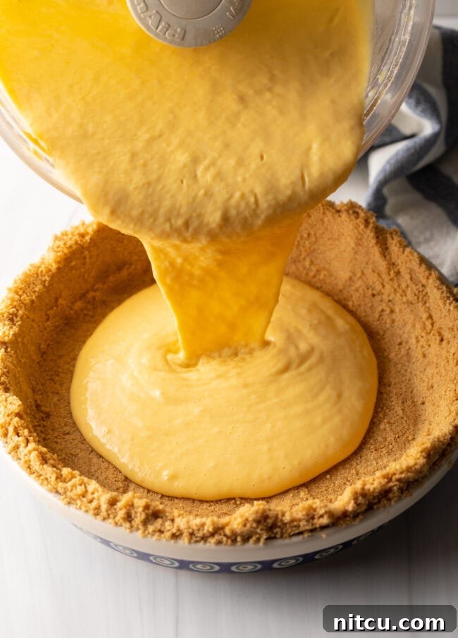 The smooth, creamy mango custard being poured into the pre-made graham cracker pie crust, filling it beautifully.