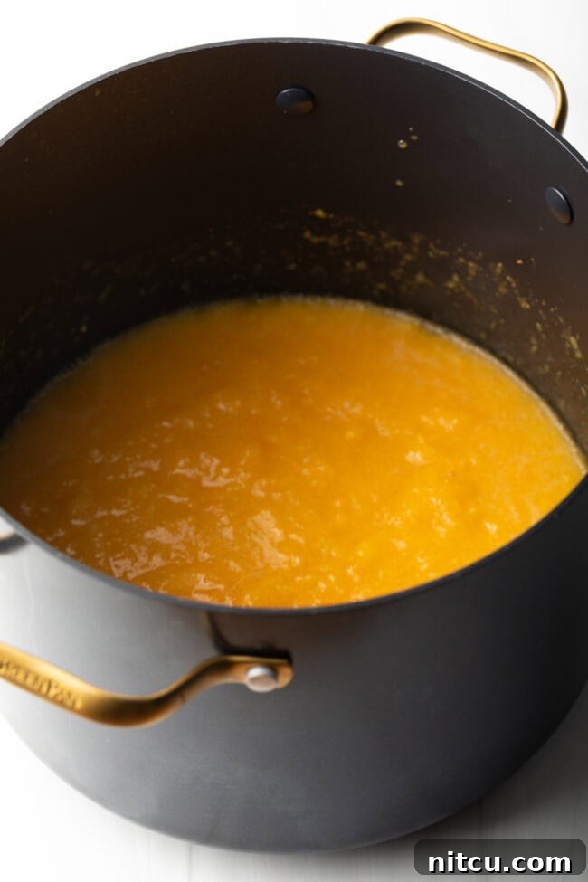 Large black cooking pot with cooked peach preserves simmering.
