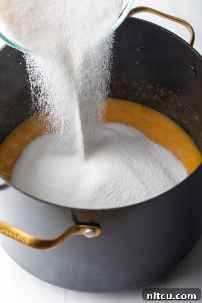 Adding a large quantity of sugar to a pot of simmering peaches.