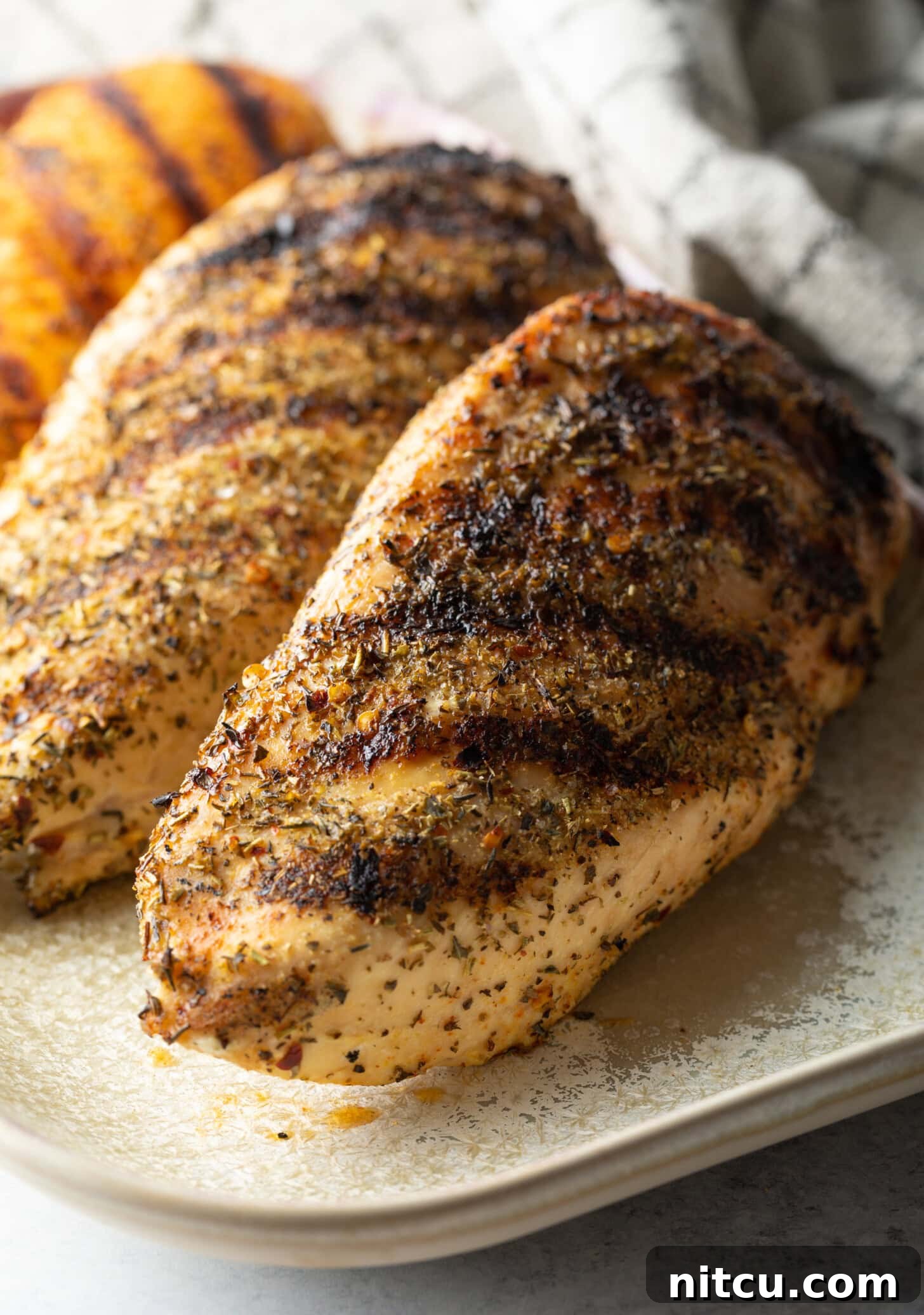 Signature Chicken Seasoning 2 Top down view two whole chicken breasts seasoned and grilled, resting on a white plate.