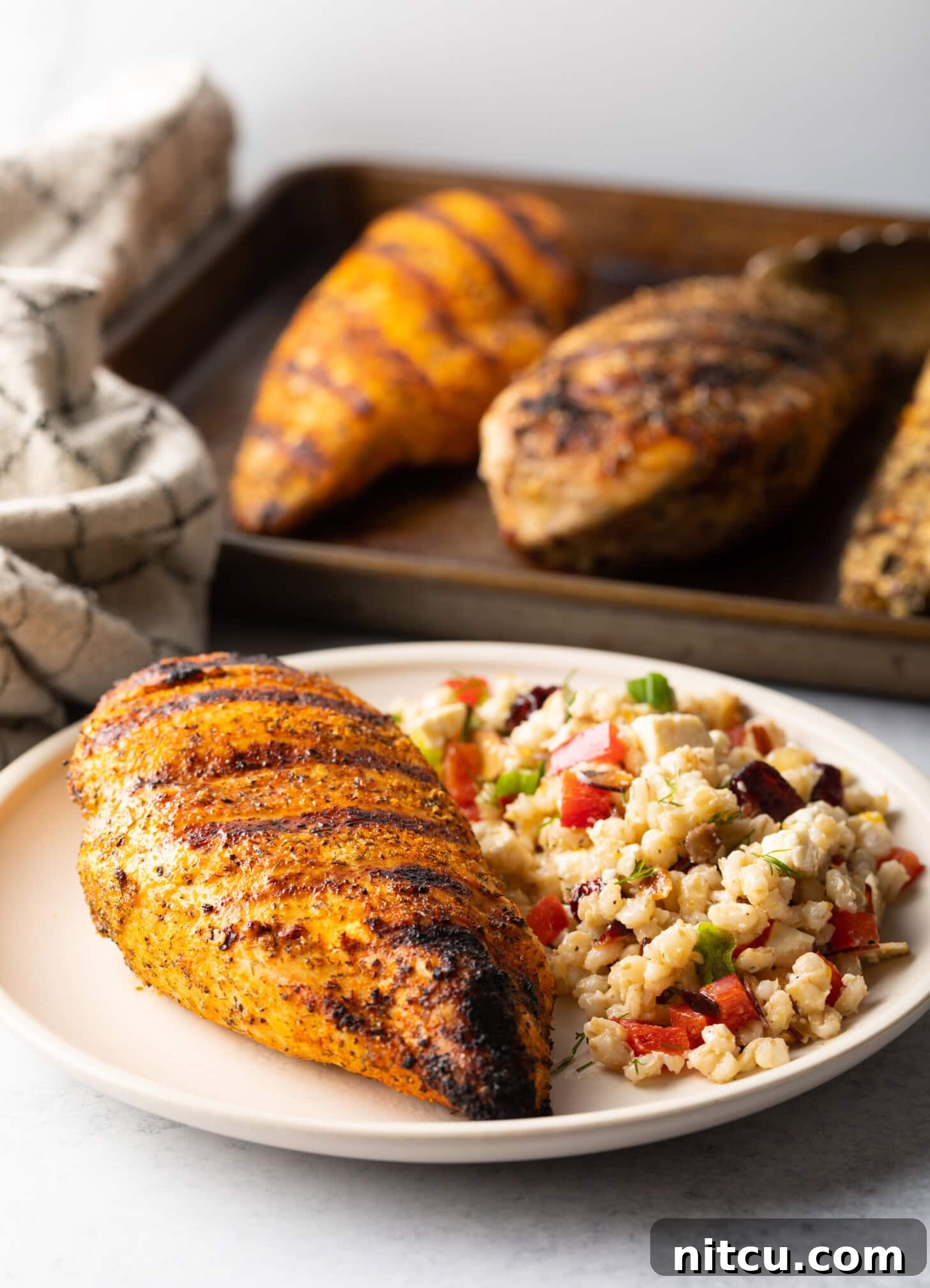 Signature Chicken Seasoning 10 One whole chicken breast seasoned and grilled, resting on a white plate next two a side of bean salad.