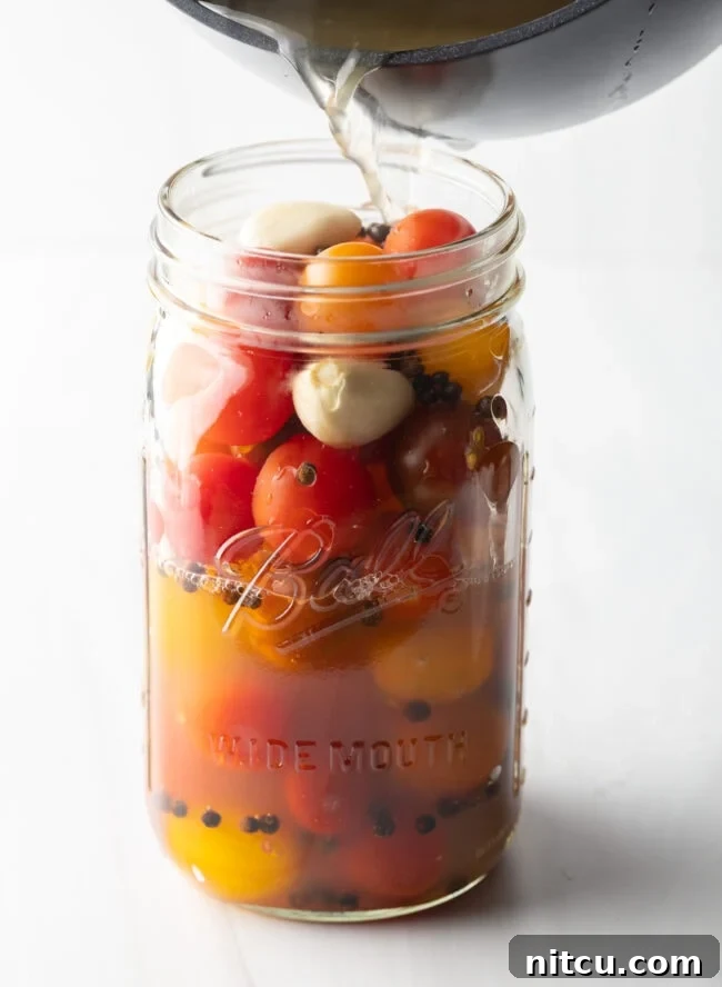Tangy Tomato Preserves 11 Adding pickling liquid to large glass jar filled with small red and yellow tomatoes.