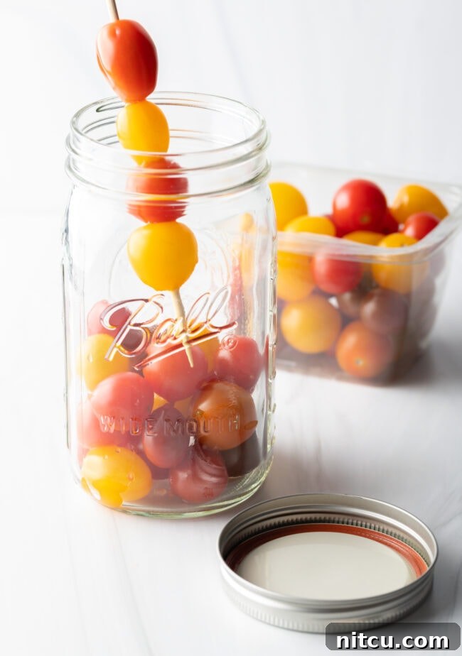 Tangy Tomato Preserves 7 Adding small yellow and red cherry tomatoes to a large glass ball jar.