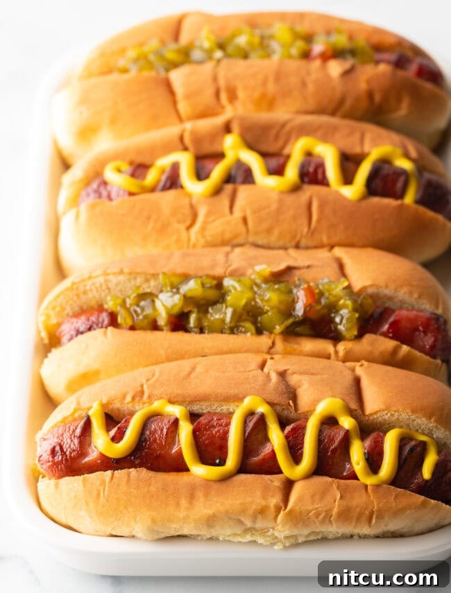 Crispy Air-Fried Franks 2 Four hotdogs in buns placed side by side on a white rectangle plate. The toppings alternative between relish and zigzag of mustard.