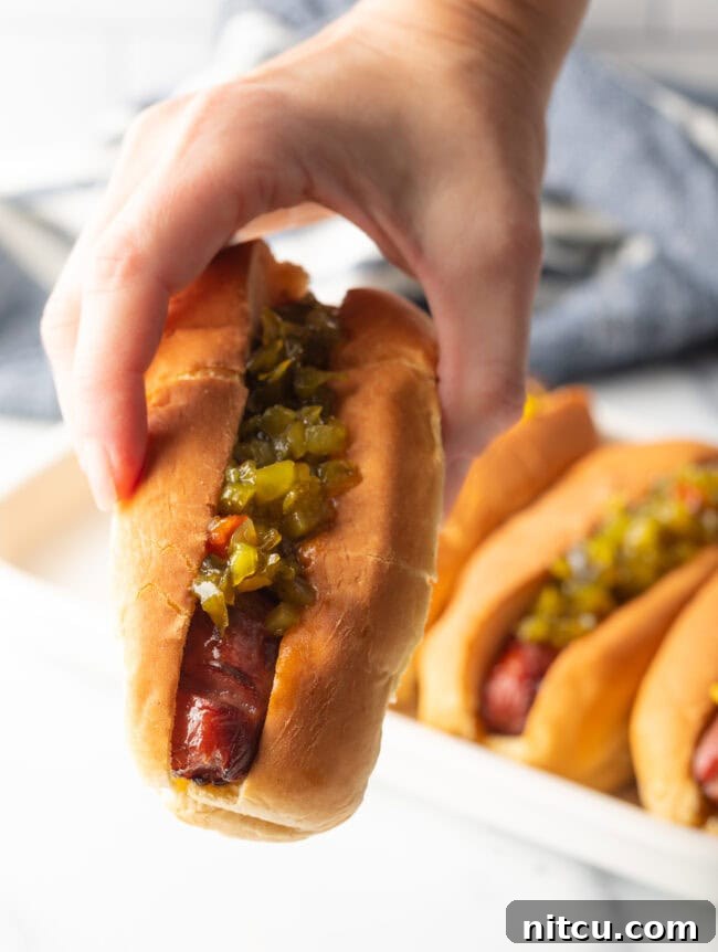 Crispy Air-Fried Franks 11 Hand holding air fried hot dog in bun dressed with relish, towards camera.