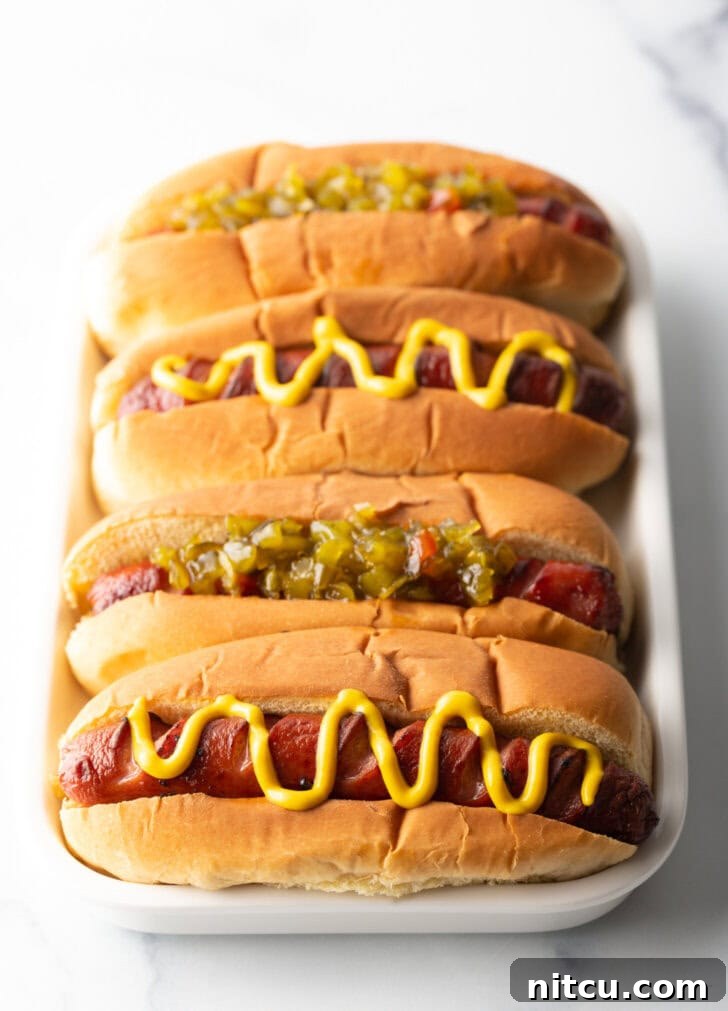 Crispy Air-Fried Franks 8 Four hotdogs in buns placed side by side on a white rectangle plate. The toppings alternative between relish and zigzag of mustard.