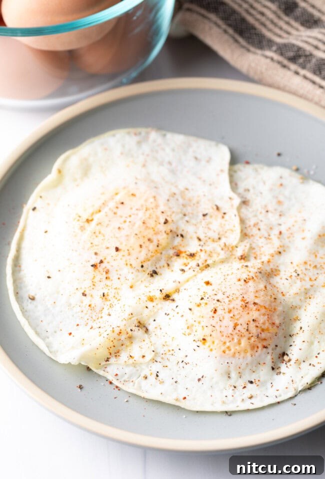 Mastering Over Easy Eggs 2 Two cooked eggs over easy on a light blue plate, sprinkled with spices.