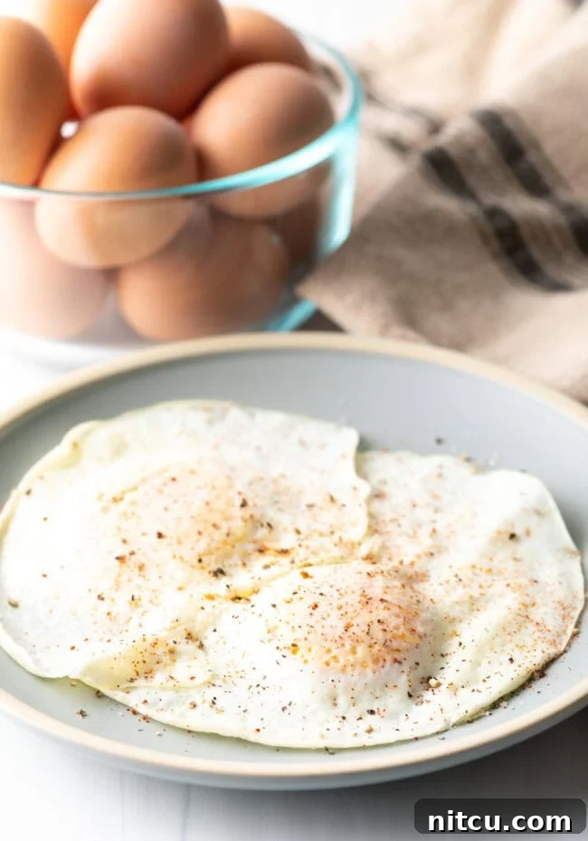 Mastering Over Easy Eggs 12 Two cooked eggs over easy on a light blue plate, sprinkled with spices.
