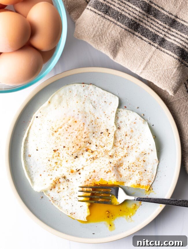 Mastering Over Easy Eggs 14 Fork cutting into the soft yolk of a gently over easy fried egg, on a light blue plate.