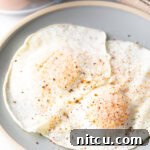 Two cooked eggs over easy on a light blue plate, sprinkled with spices.