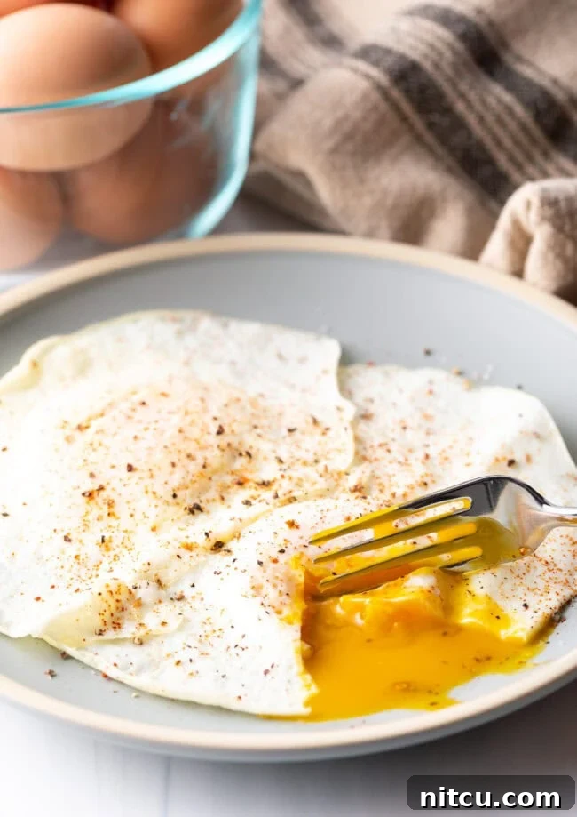 Mastering Over Easy Eggs 16 Fork cutting into the soft yolk of a gently over easy fried egg, on a light blue plate.